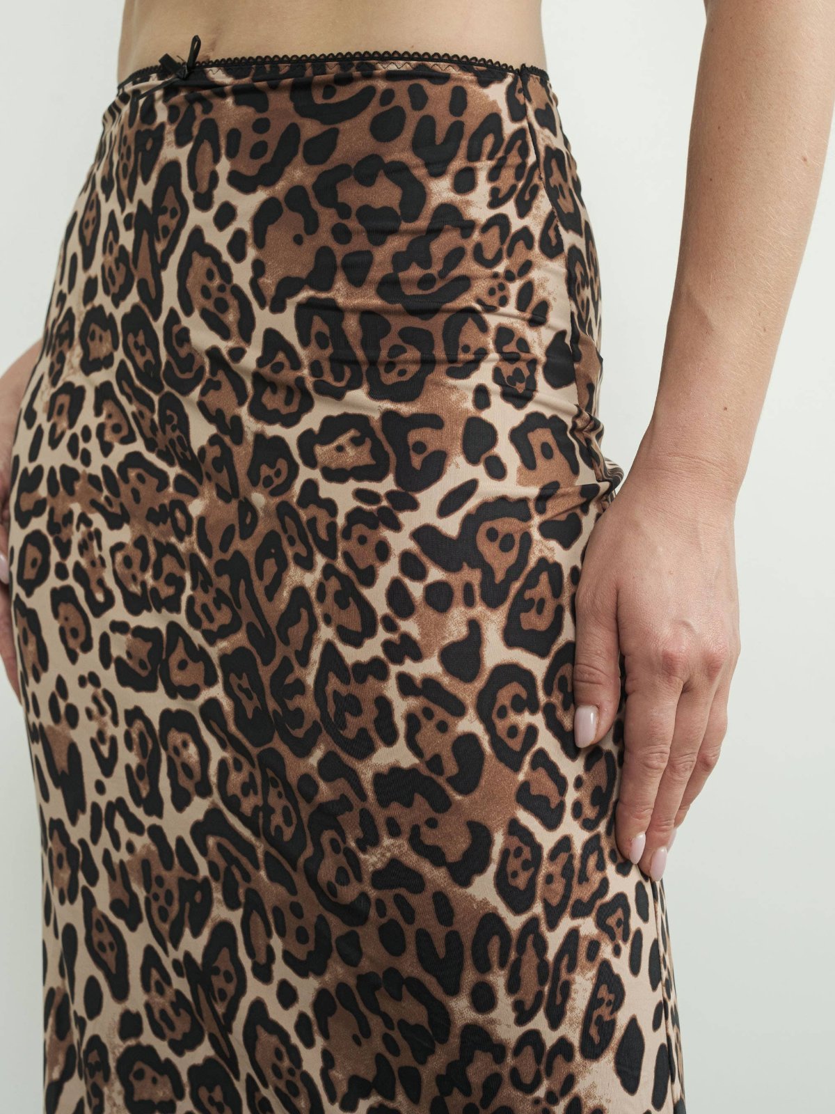 Model wearing a mid-waist leopard print knit maxi skirt with lace trim at the waistband and a small bow. The skirt is form-fitting around the hips and flares slightly towards the hem, creating a flowy silhouette. The model pairs it with pointed black shoes.